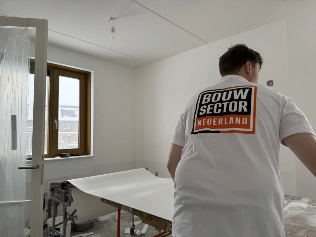 Renovlies behanger van Bouwsector Nederland rolt een baan vlies uit over de plaktafel in een nieuwbouwkamer