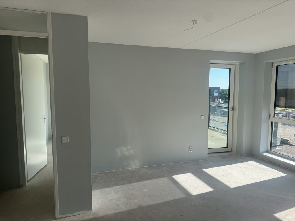 Nieuw appartement met betonvloer en strak afgewerkte lichte wanden, uitzicht op een bouwterrein