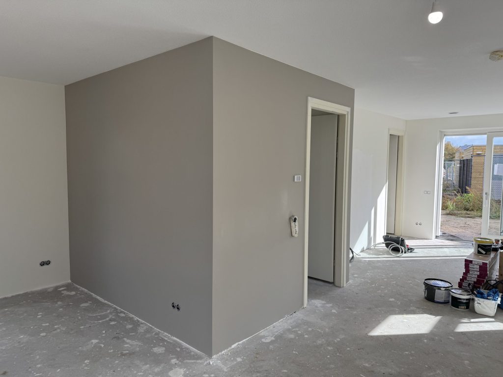 Nieuwbouwwoning waarin een wand net grijs is afgewerkt, met verfemmers op de betonvloer